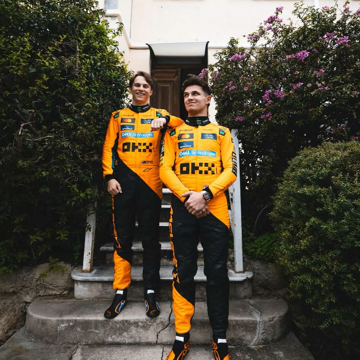 Oscar and Lando in McLaren 2025 orange F1 racing suits standing on steps outdoors.