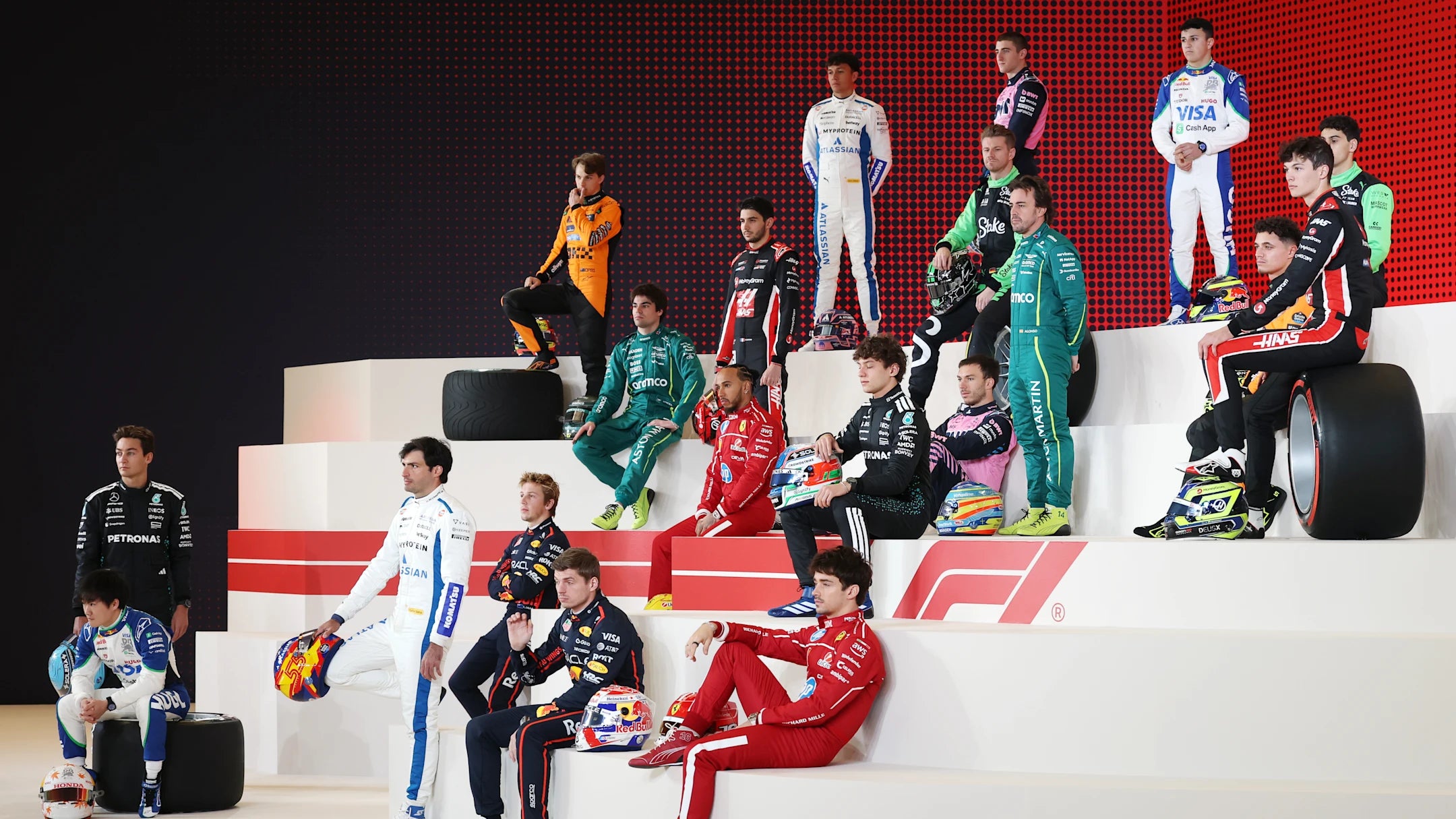 Multiple Formula 1 drivers in 22025 F1 racing suits on a podium with a red digital background
